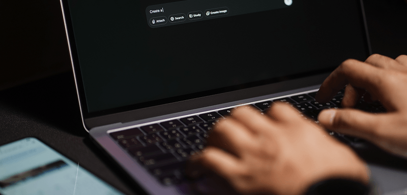 Hands typing on a laptop keyboard with a mobile phone beside it