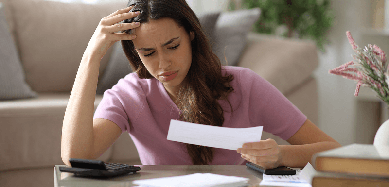 Worried woman holding a letter with calculators and paperwork on a table