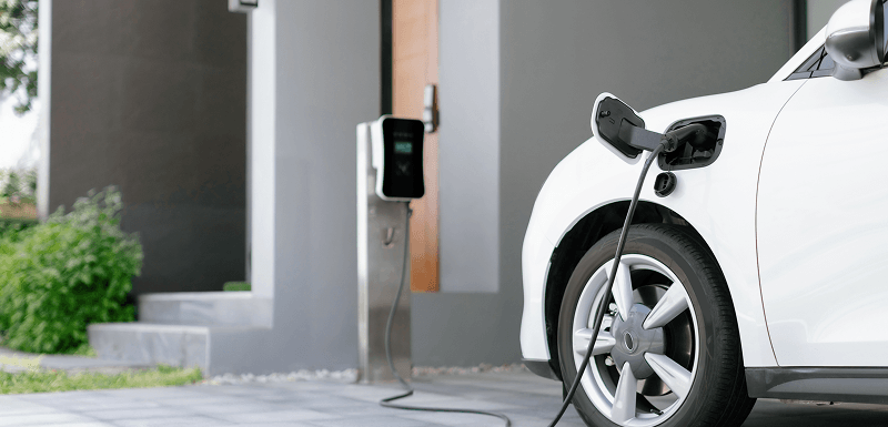 White electric car plugged into a charging point beside a house
