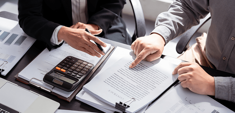 Two people review paperwork at a desk with a calculator and charts